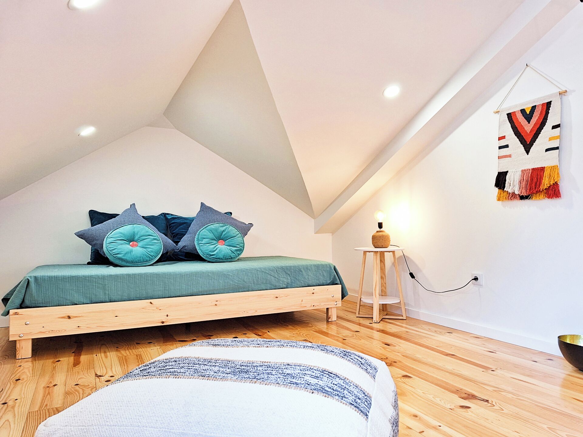 Ein modernes Schlafzimmer im Loft-Stil mit schrägem Dach, einem Bettgestell aus Holz und einer grünen Bettdecke.