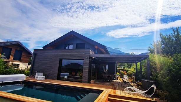 Una casa moderna con piscina, terraza de madera y zona de estar exterior.