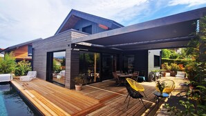 Una casa moderna con terraza de madera, piscina y mobiliario exterior.