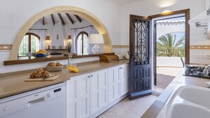 Une cuisine moderne avec des meubles blancs, une grande fenêtre en arc de cercle et une vue sur l’extérieur.