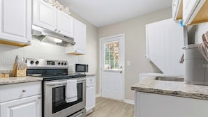 A modern kitchen with white cabinetry, stainless steel appliances, and a granite countertop. - The Tulip in Midtown (Mobile)