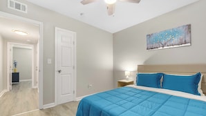 A bedroom with a large bed, a ceiling fan, a painting on the wall, and a door leading to another room. - The Tulip in Midtown (Mobile)