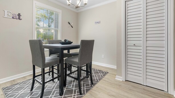 A dining area with a table and four chairs, a chandelier, a window with blinds, and a closed closet. - The Tulip in Midtown (Mobile)