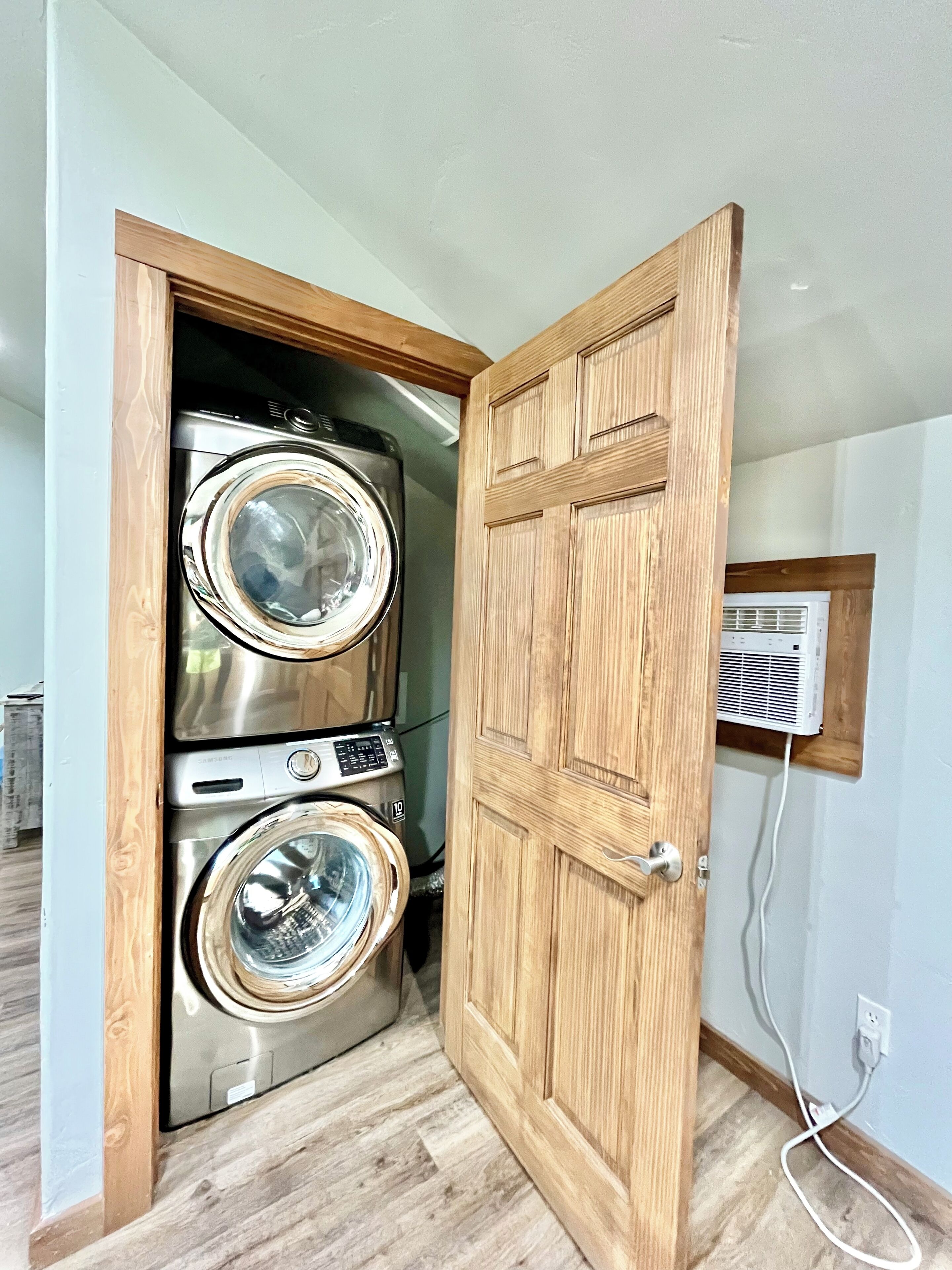 A laundry room with two stacked front-loading washing machines and a wooden door.