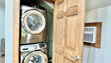 A laundry room with two stacked front-loading washing machines and a wooden door.