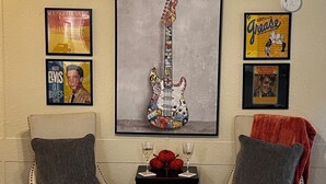 A room with two chairs, a small table with two wine glasses and decorative items, and framed posters on the wall.