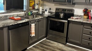 A modern kitchen with stainless steel appliances, grey cabinets, and a wooden floor.