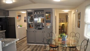 A compact kitchen with a refrigerator, coffee maker, and a glass-top dining table with chairs.