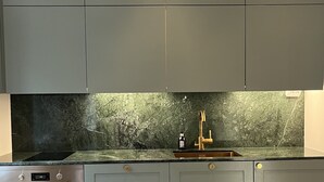 A kitchen with grey cabinets, a black countertop, and a marble backsplash. - High-end, quiet, downtown home (Helsinki)