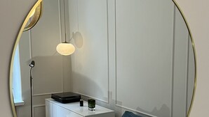 A room with a round mirror, a white desk with a lamp, a blue sofa, and a patterned pillow. - High-end, quiet, downtown home (Helsinki)