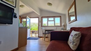 A living room with a red sofa, a television, and a dining area with a table and chairs. - Self-catering holiday Chalet in Cornwall (Saint Merryn)