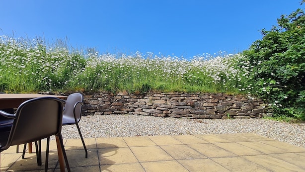 An outdoor patio with a stone wall, a table, and chairs. - Self-catering holiday Chalet in Cornwall (Saint Merryn)