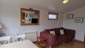 A living room with a red sofa, a white table, and a lamp. There is a mirror on the wall and a window with blinds. - Self-catering holiday Chalet in Cornwall (Saint Merryn)