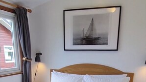 A neatly made bed with white linens and a folded towel, a framed picture of a sailboat on the wall, and a bedside lamp. - Self-catering holiday Chalet in Cornwall (Saint Merryn)