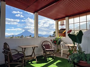 A covered patio with a view of a mountain, two wooden chairs, a table, and potted plants. - Spacious Family Apartment with Mountain Views in Panajachel (Panajachel)