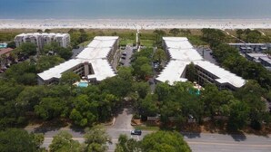 Vista aérea de um hotel com vista para a praia, com vários edifícios de telhado plano e rodeado por vegetação.