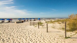 Uma praia de areia com guarda-sóis azuis e espreguiçadeiras.