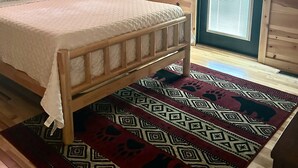 A wooden cabin bedroom with a bed, a window, and a patterned rug.