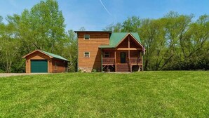 A two-story log cabin with a green roof, a front porch, and a separate garage.
