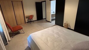 Een slaapkamer met een groot bed, een stoel, een kledingkast en een badkamer, zichtbaar door een geopende deur.