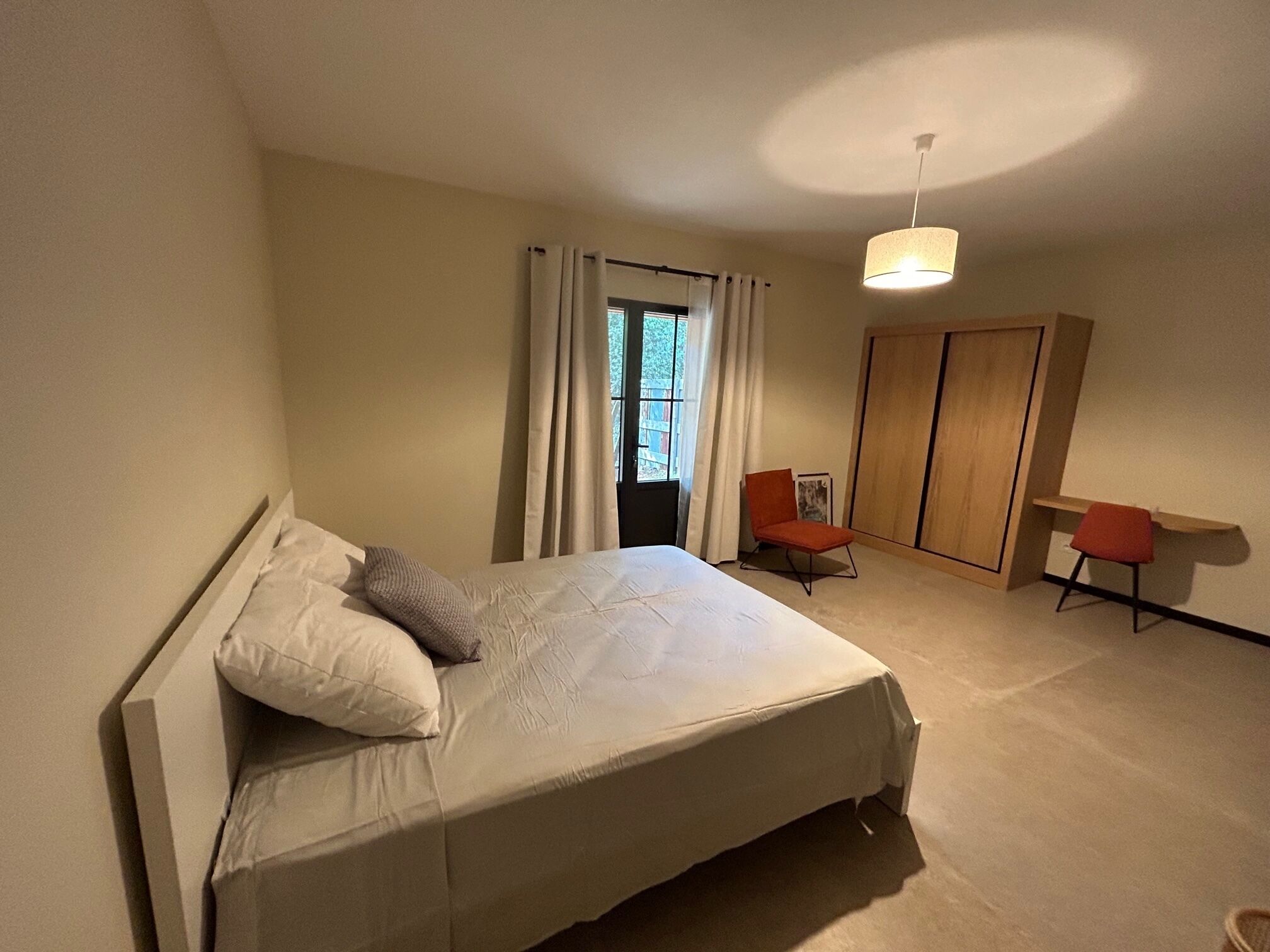 Quarto com cama, duas cadeiras, escrivaninha, guarda-roupa e janela com cortinas.