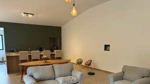 Een moderne woonkamer met een grijze bank, een ronde salontafel, en een eethoek met een houten tafel en stoelen.