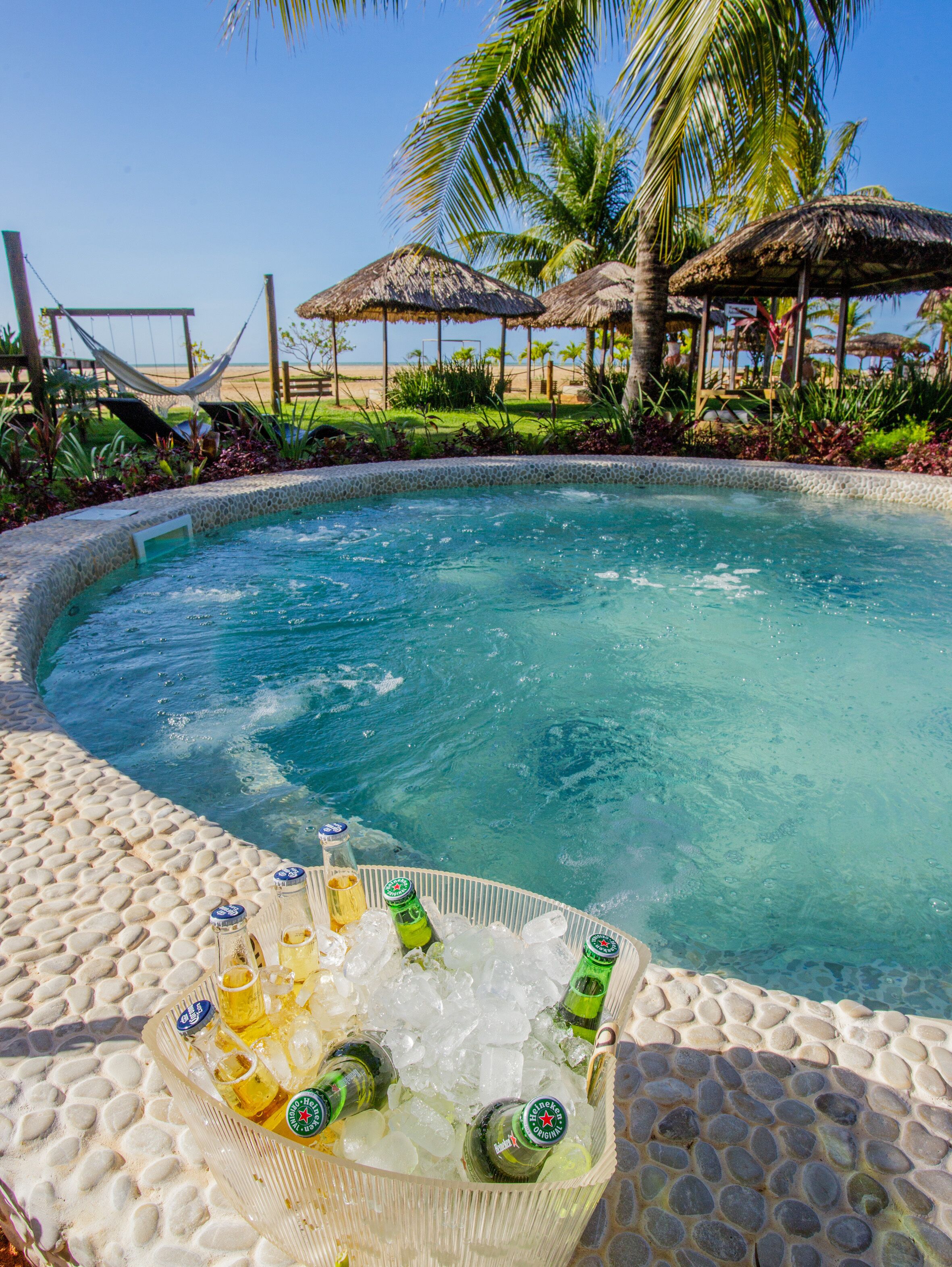 Un espace piscine aménagé dans un décor tropical, avec des palmiers et une structure surmontée d’un toit de chaume.