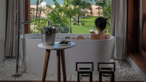 Eine Badewanne mit Blick auf einen Strand, ein Eimer und ein Glas Wein.