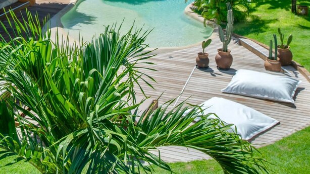 Ein Poolbereich mit Holzterrasse, Liegestühlen und Blick auf Strand und Meer.