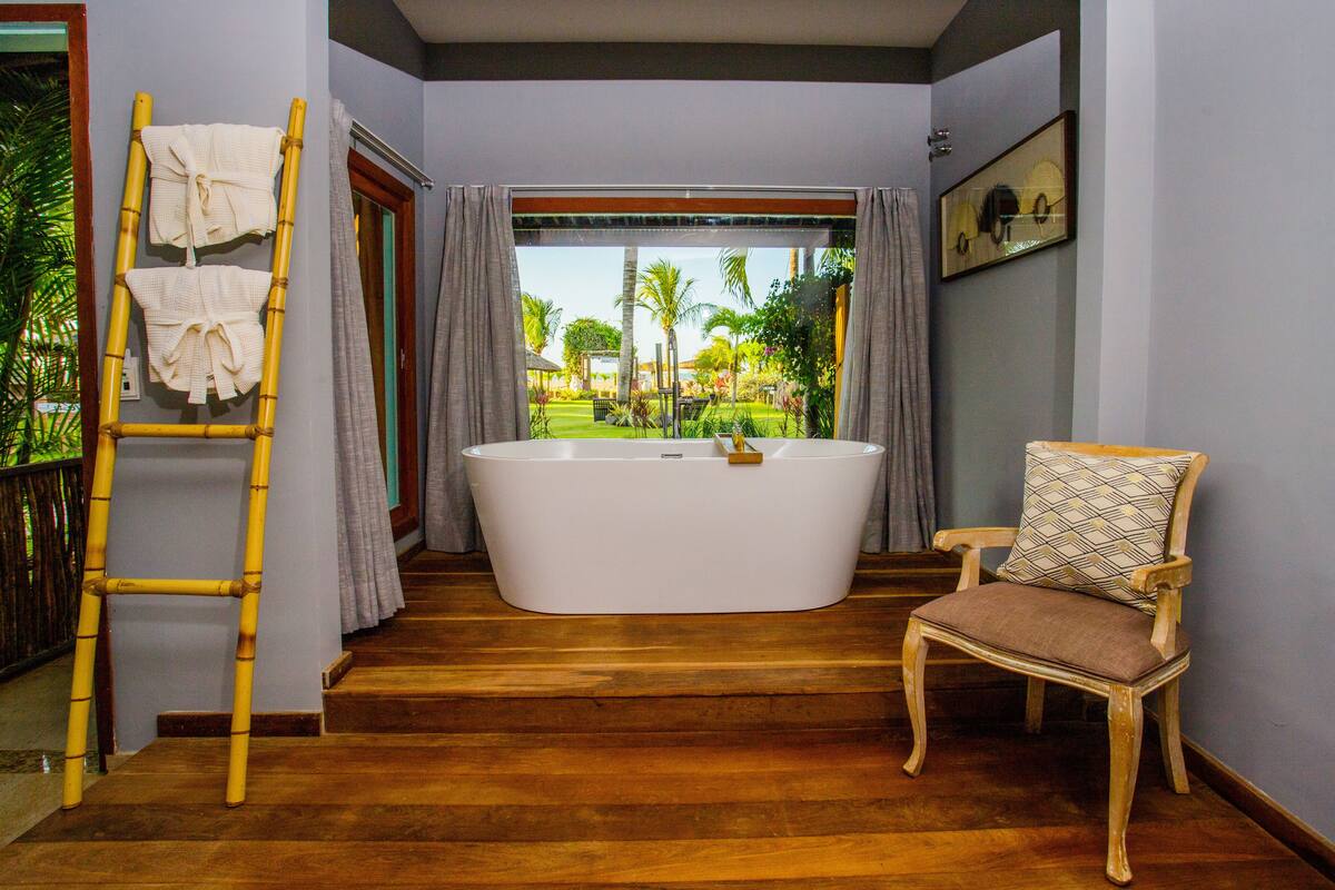 Un baño con una bañera grande, una silla de madera y una escalera de bambú con toallas.