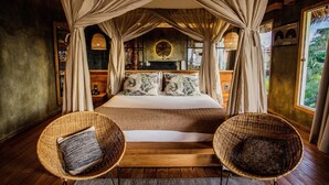 Ein Schlafzimmer mit Baldachinbett, zwei Korbstühlen, Holzboden und Blick ins Freie.