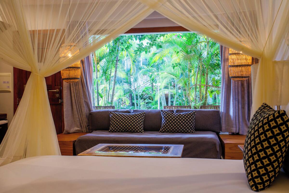 Un dormitorio con cama, ventana con vistas a vegetación y dosel.