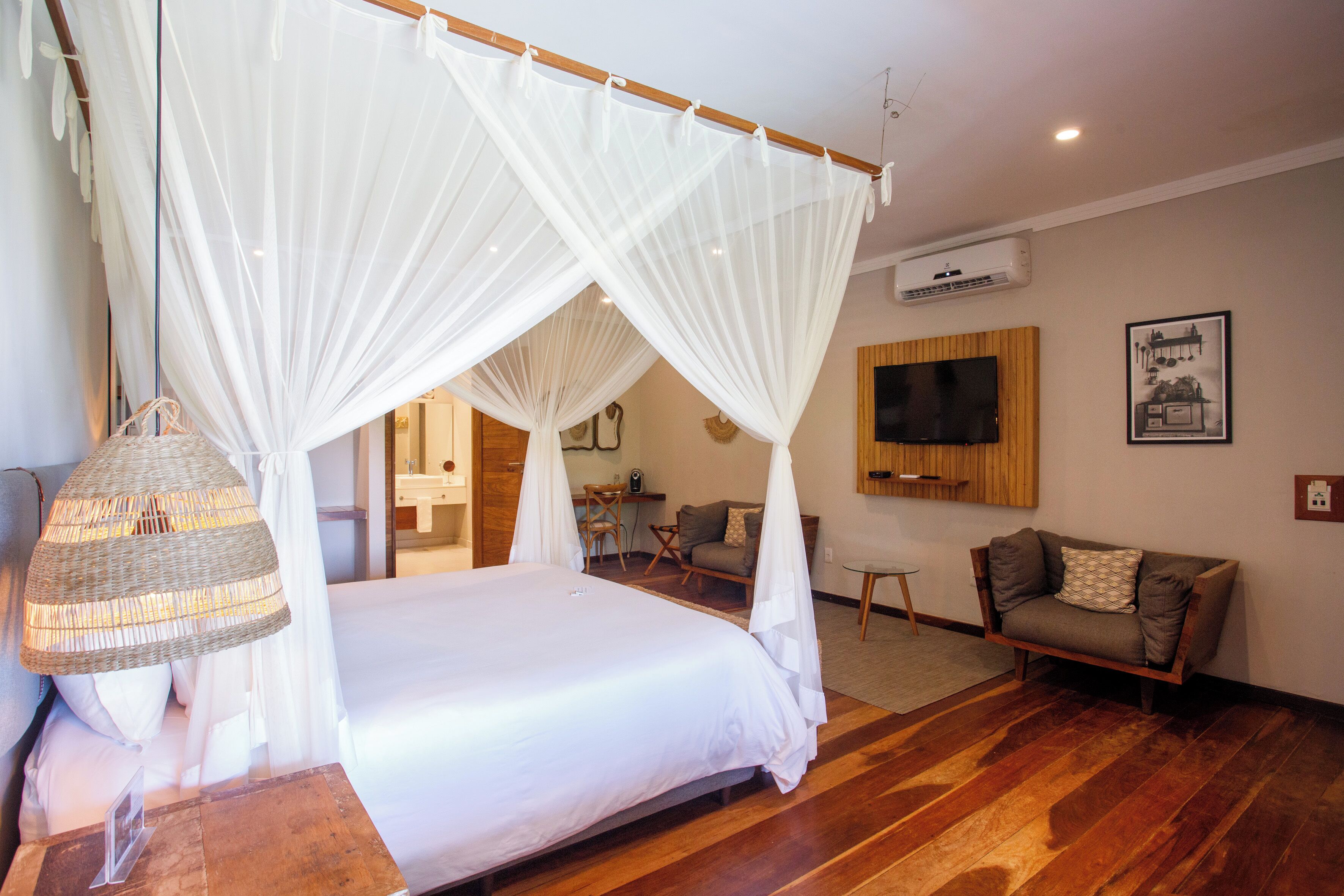 A bedroom with a four-poster bed, a television, a sofa, and a wicker lamp.