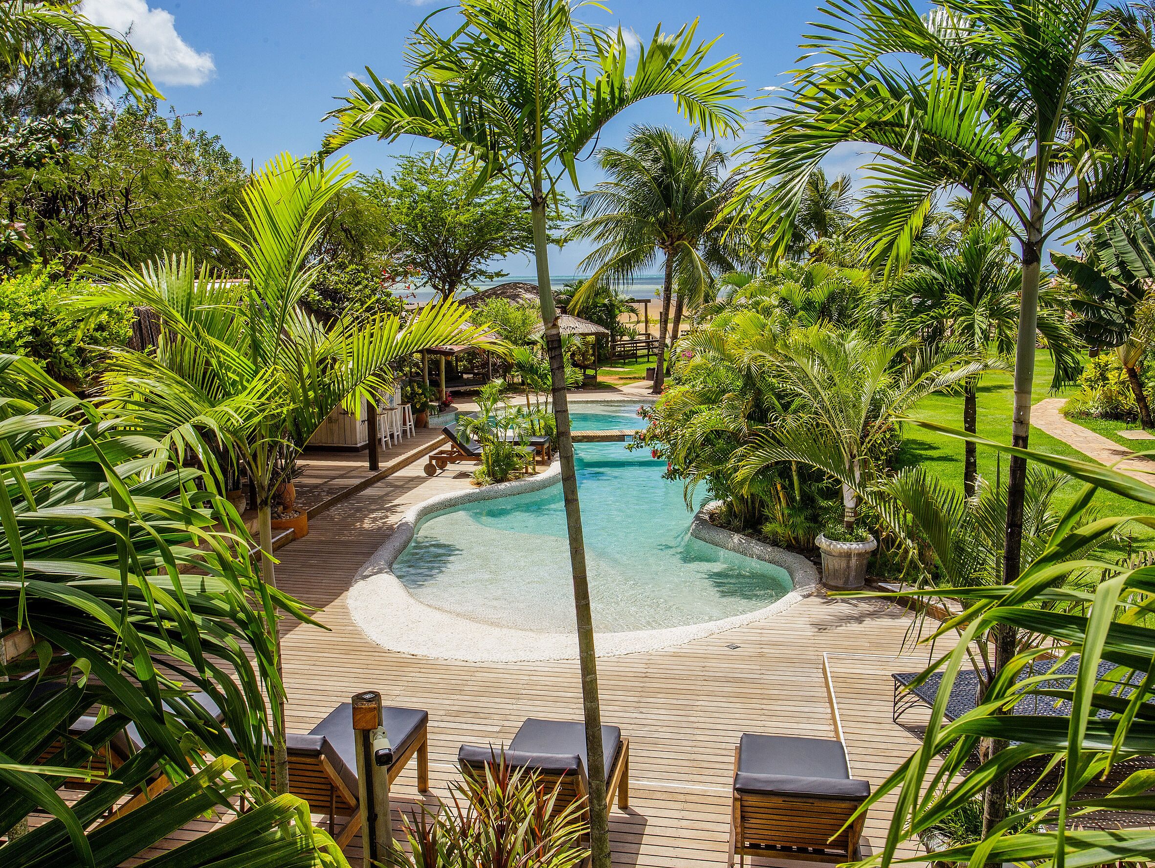 A tropical resort with a swimming pool, lounge chairs, and lush greenery.