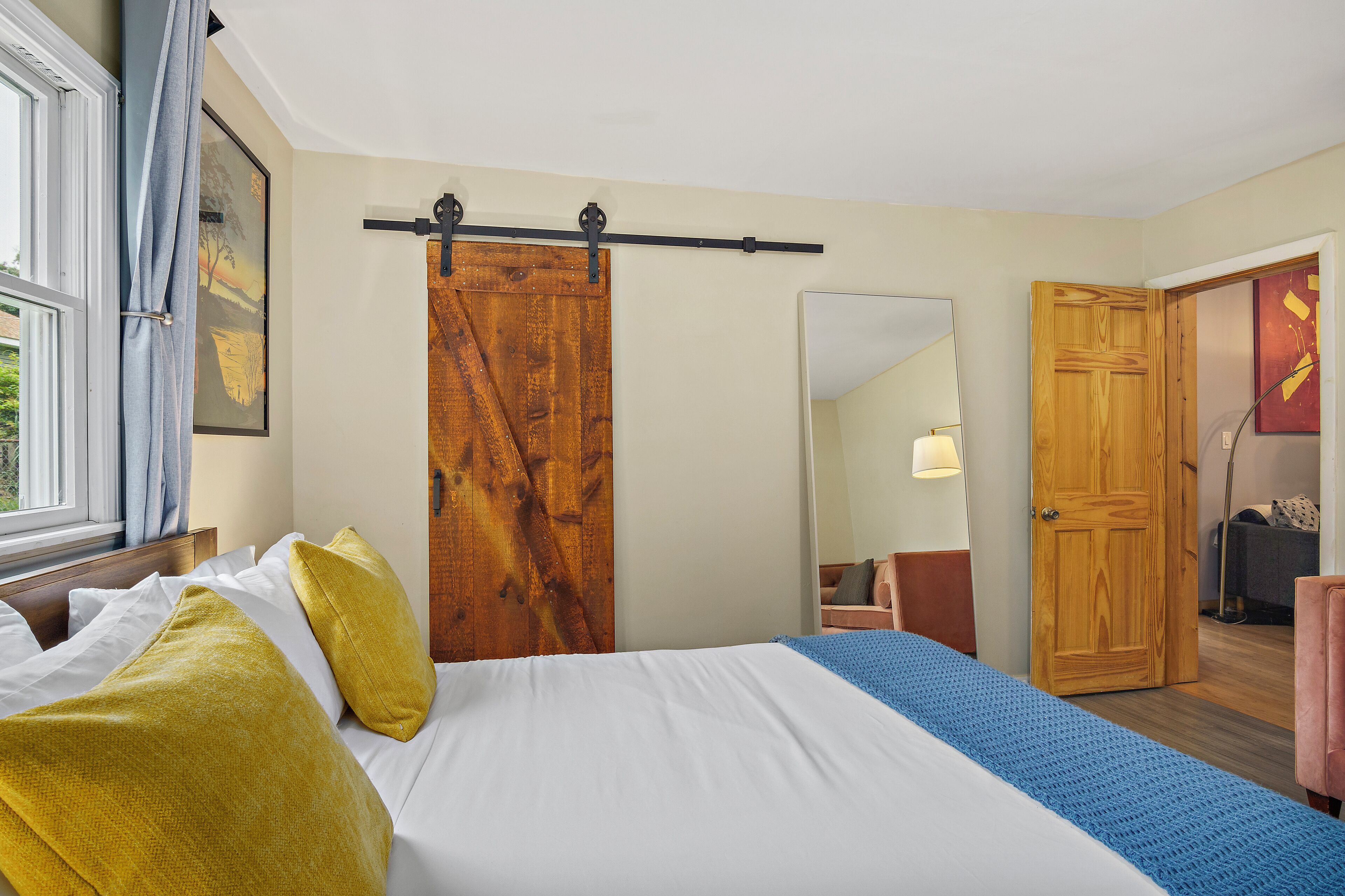 Ein Schlafzimmer mit einem Bett, einer Holztür, einem Spiegel und einem Fenster mit Vorhängen.