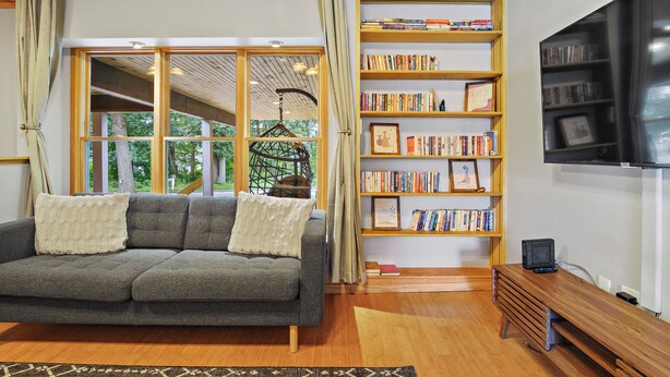 A cozy living room with a grey sofa, wooden bookshelves, and a flat-screen TV. - 4BR House near Casinos & Beach With In Law Suite (Preston)