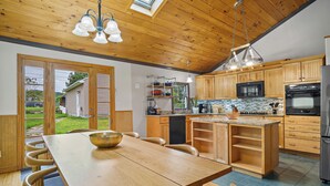A modern kitchen with wooden cabinets, a central island, and a dining area with a wooden table and chairs. - 4BR House near Casinos & Beach With In Law Suite (Preston)