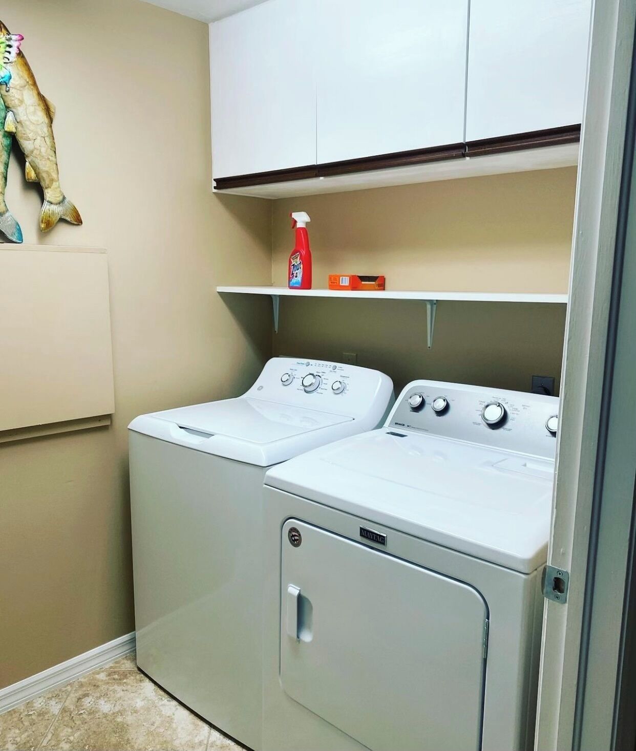 A laundry room with two front-loading washing machines, a shelf with a bottle of detergent, and a decorative item on the wall.