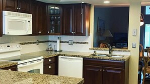 A kitchen with granite countertops, dark wooden cabinets, a microwave, stove, dishwasher, and a ceiling fan. - Large 2 br n loft, 5 miles from downtown Naples 5th Avenue! On golf course (Naples)