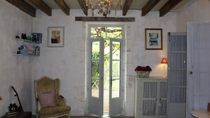 A room with a wooden ceiling, a chandelier, a chair, a door, and a small table with a lamp. - VILLA CHEZ JENNY (Saint Privat en Périgord)