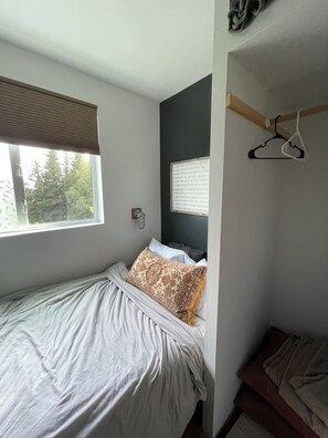 Un dormitorio con cama, ventana, luz empotrada en la pared y perchero.