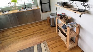 A modern kitchen with a flat-screen TV, wooden shelves, a microwave, and a refrigerator. - Fireweed Hollow Junior - Cozy and cute modern cabin (Homer)