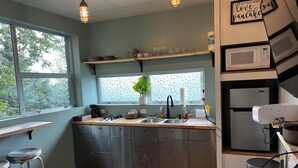 A modern kitchen with stainless steel appliances, a wooden countertop, and a window with a view of trees. - Fireweed Hollow Junior - Cozy and cute modern cabin (Homer)