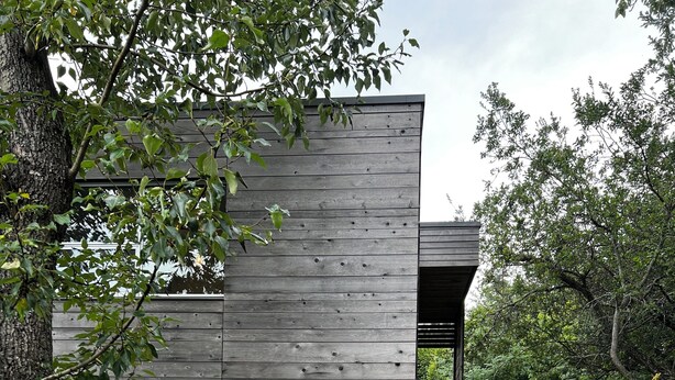A modern house with a wooden exterior, a wooden door, and a staircase leading to an upper level. - Fireweed Hollow Junior - Cozy and cute modern cabin (Homer)