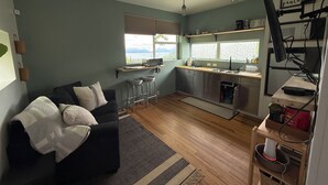 A compact living space with a sofa, kitchen area, and a view of the outdoors. - Fireweed Hollow Junior - Cozy and cute modern cabin (Homer)