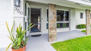 A modern building with a white exterior, numbered 350, featuring a welcoming entrance with a potted plant and a stone pillar. - Waterfront Oasis – Private Heated Pool & Waterfall Hot Tub (Pompano Beach)