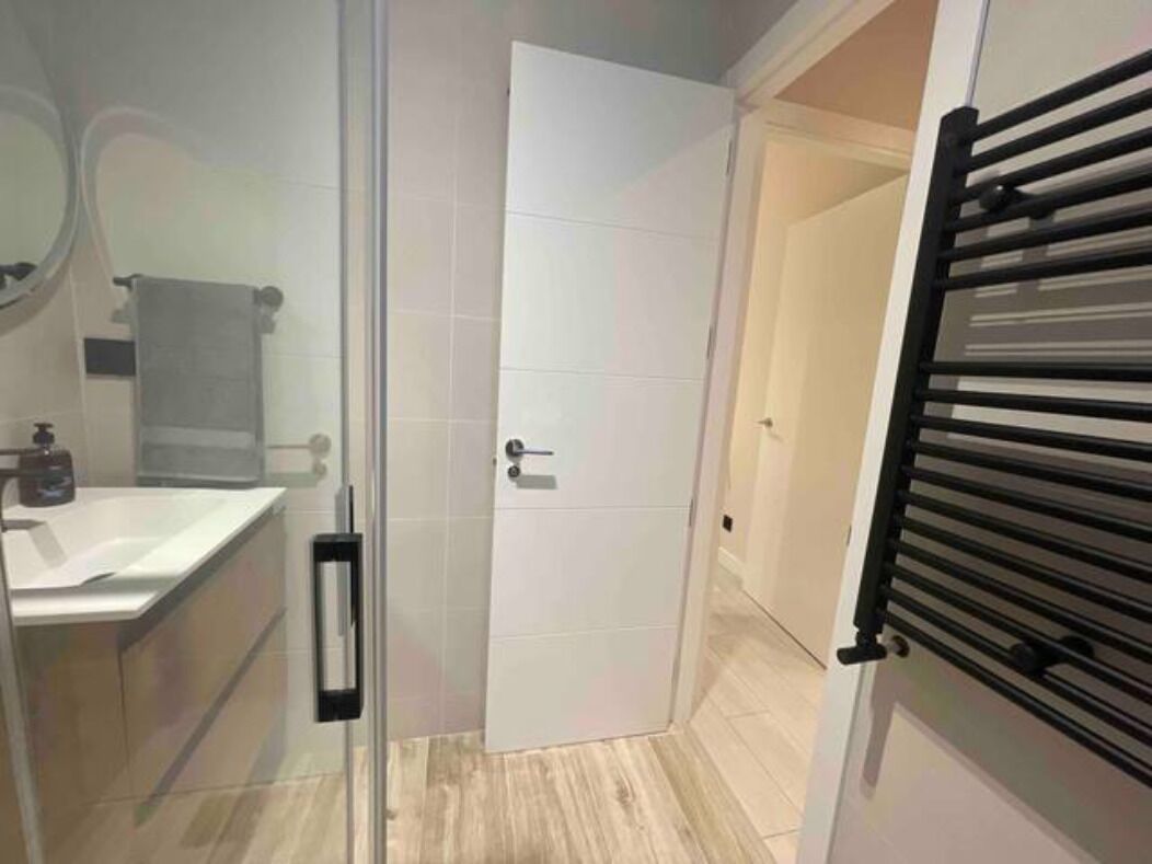 A modern bathroom with a glass shower enclosure, a white sink, and a towel rack.