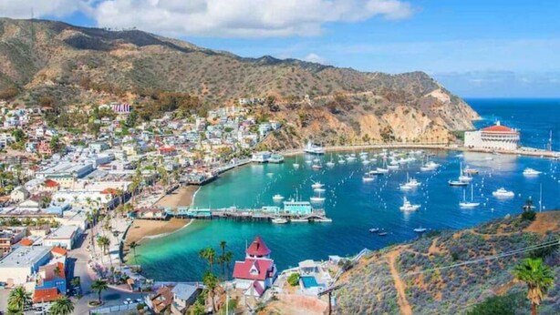 Une ville côtière dotée d’un port de plaisance, de bâtiments et bordée par une chaîne de montagnes.