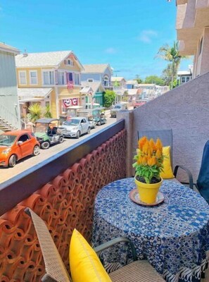 Enjoy the view of the vibrant street scene from this balcony with a small table and chair.