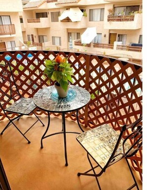 Un balcon avec une table ronde et deux chaises, un pot de fleurs et une clôture en treillis.